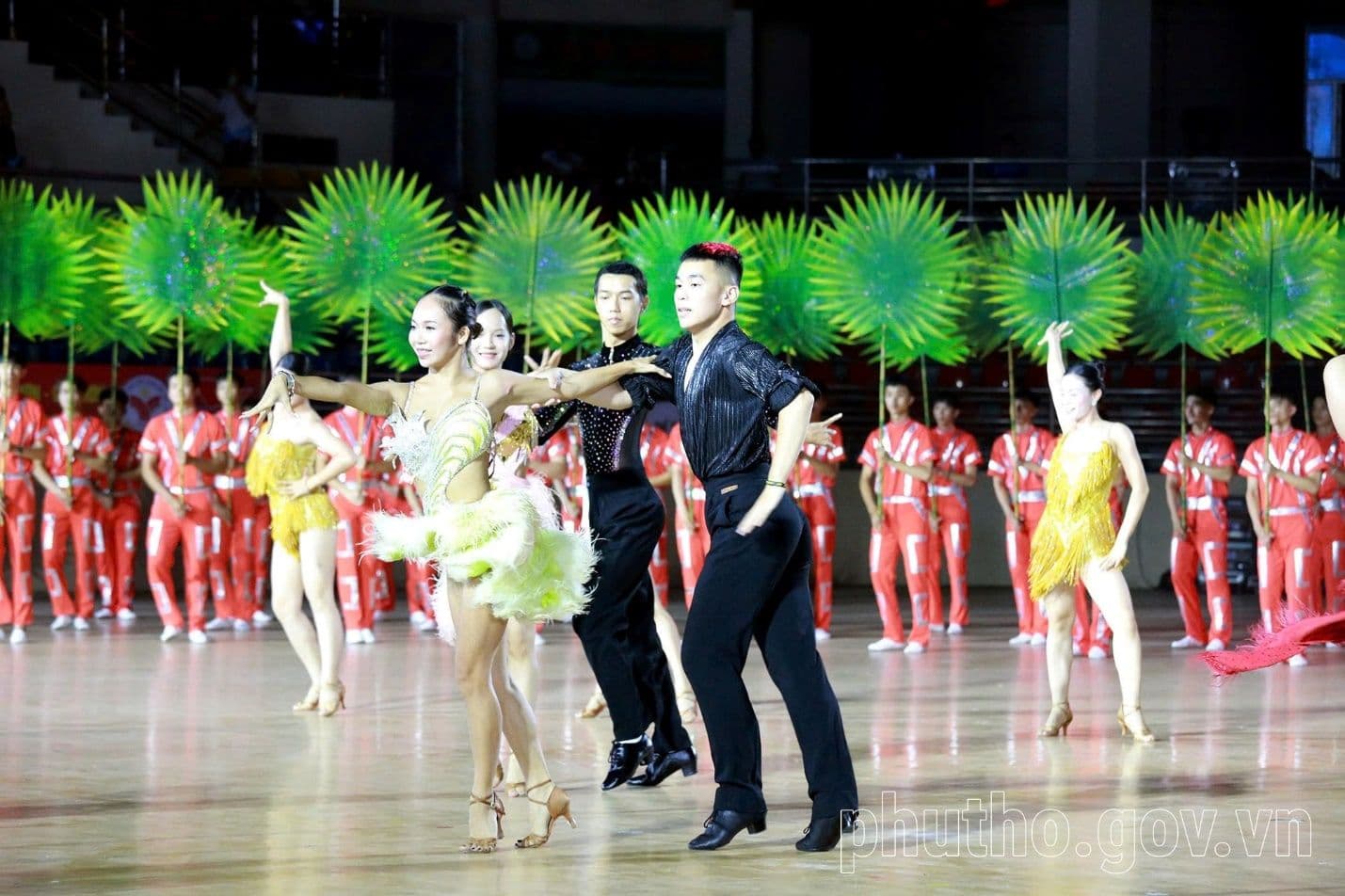 Cặp vận động viên khiêu vũ thể thao biểu diễn trước khối đồng diễn cầm lá cọ