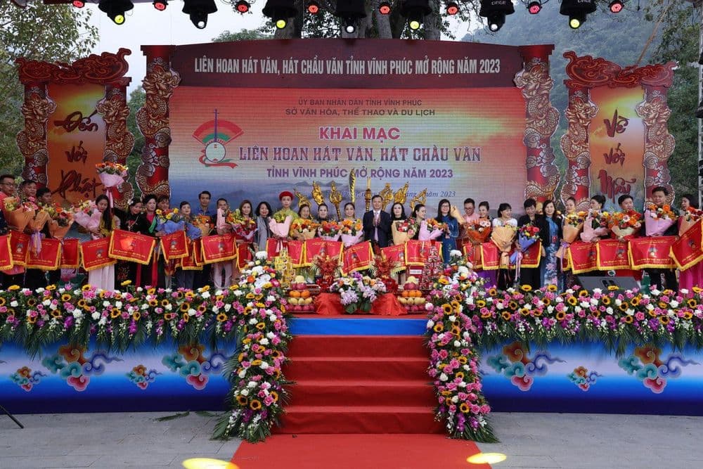 Sân khấu khai mạc Liên hoan hát Văn, hát Chầu văn tỉnh Vĩnh Phúc mở rộng năm 2023 tại Tây Thiên: phông LED, cổng trang trí hình rồng hai bên, đèn moving head treo phía trên, đại diện các câu lạc bộ cầm cờ lưu niệm và hoa