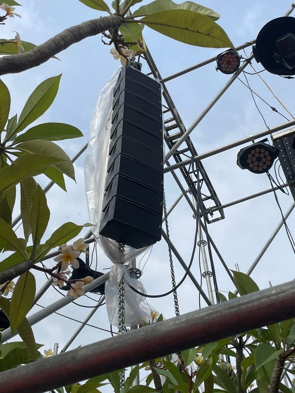 Cụm line array NEXO GEO M6 chín thùng treo bằng tời xích trên khung giàn giáo sân khấu ngoài trời, có bọc chống mưa, do BOS Entertainment dựng