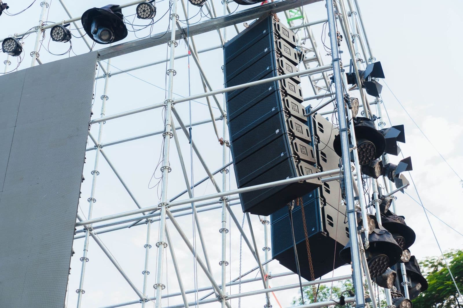 Dàn loa line array NEXO treo trên cột giàn bên cánh sân khấu ngoài trời, xen kẽ đèn sân khấu