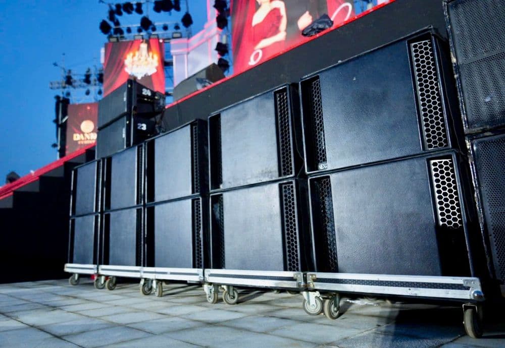 Hàng sub NEXO LS18 của BOS Entertainment xếp chồng hai tầng trên xe đẩy dưới sân khấu ngoài trời, phía trên là loa GEO S12 và màn LED